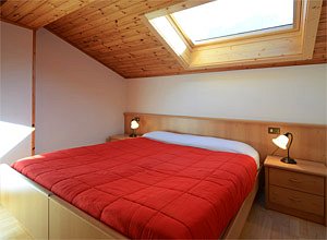 Appartamento a Soraga di Fassa. La camera matrimoniale con finestra a tetto dove, stando a letto, si può ammirare un meraviglioso cielo stellato o la bella Cima Dodici. 
Sulla destra si intravede il bagno -finestrato- completo di vasca e degli altri accessori.