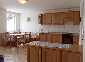 Appartamento a Moena. L'angolo cucina, molto spazioso e illuminato, è fornito di arredamenti rustici e curati.