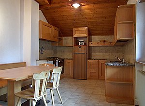 Appartamento a Campitello di Fassa. Ampia cucina abitabile arricchita da tavolo con panca ad angolo, caratteristica stufa a legna e lavastoviglie.