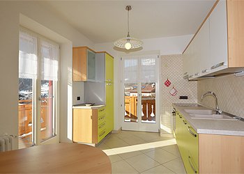 Appartamento a Moena. Il locale cucina è arredato in stile moderno sui toni del verde (o arancione). Dispone di frigorifero con freezer, lavello a 2 vasche, piano cottura in vetroceramica, forno.
Due porte finestre lo rendono molto luminoso, vi sono inoltre 2 balconi che permettono di avere una vista panoramica su Moena.