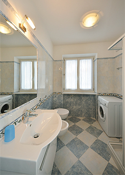 Appartamento a Moena. Il secondo bagno è arredato sui toni dell'azzurro, ha doccia, lavatrice e un caldo termo bagno scaldasalviette.