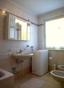Residences in Campitello di Fassa. Bathroom of the apartment nr. 2 near the bedroom on the ground floor and the living-room, with washing machine.