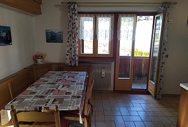Appartamento a Moena. Zona giorno caratterizzata dall'arredo in legno, tipico delle case di montagna. Vi sono due balconi che si affacciano rispettivamente verso ovest e verso sud.
