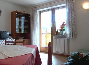 Appartamento a Soraga di Fassa. L'accogliente soggiorno con TV, divano e tavola per quattro oppure otto persone e stupendo poggiolo con panoramica verso Moena.