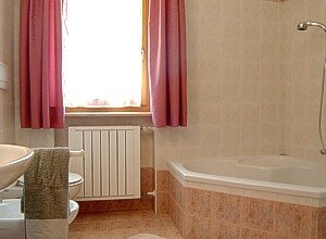 Appartamento a Soraga di Fassa. Ampio bagno di colore rosa con vasca ad angolo, doccia e lavatrice.